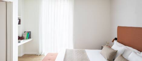 A bedroom with a bed, a nightstand, a bookshelf, and a window with curtains.