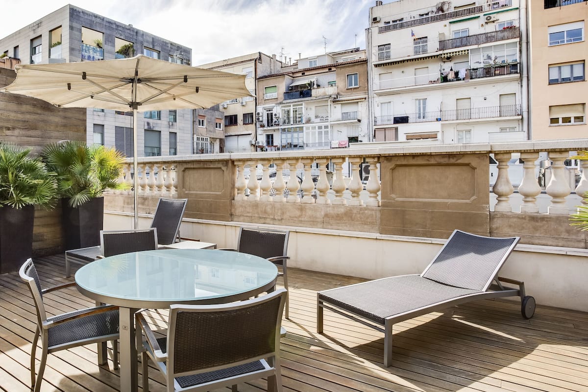 A rooftop terrace with a glass table, chairs, and a sun lounger.