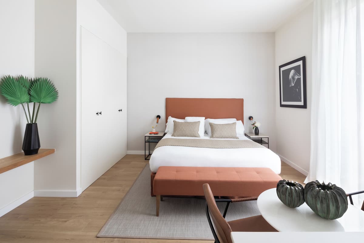 A modern bedroom with a large bed, a bedside table, a nightstand, a chair, and a small table with decorative vases.