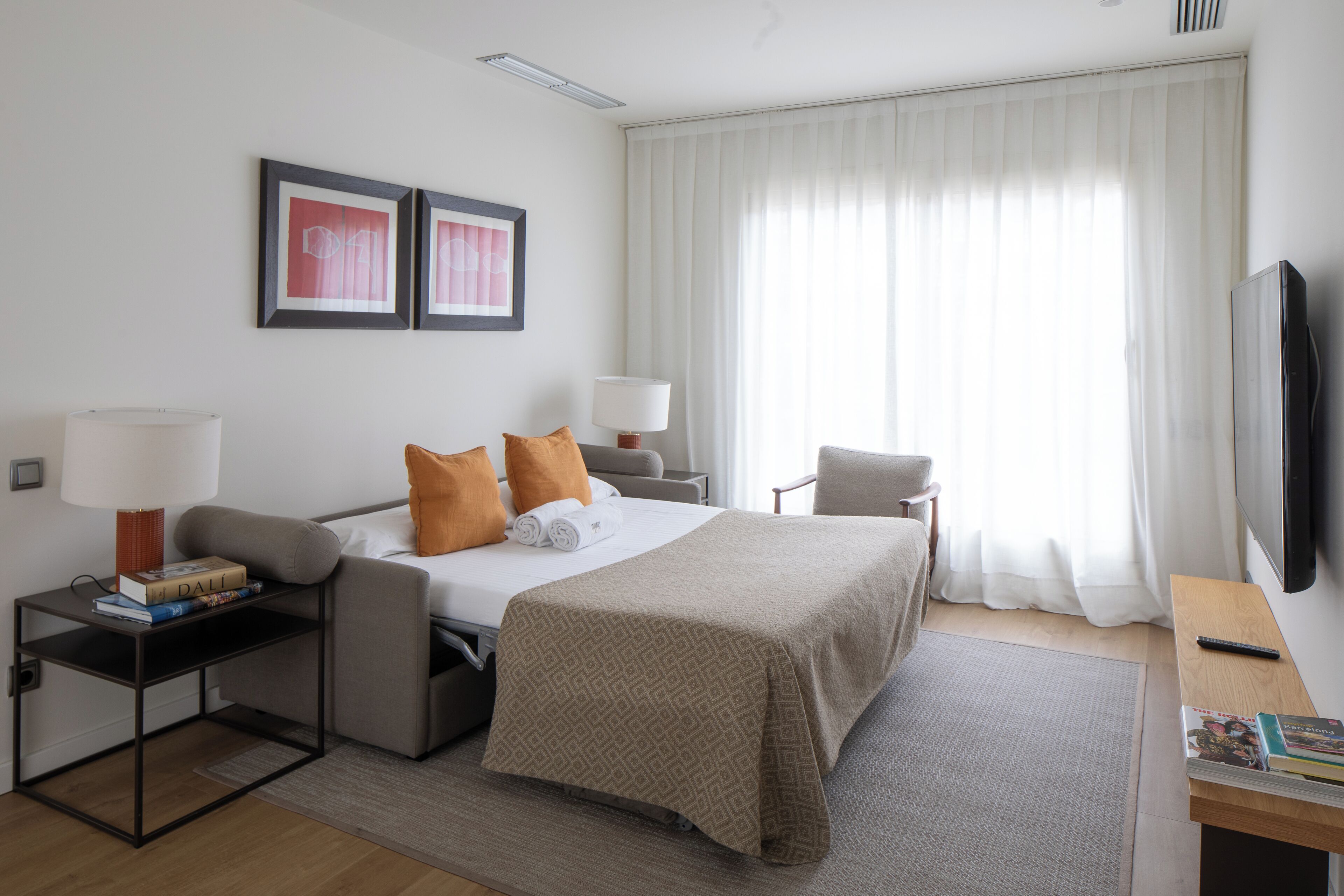 A hotel room with a bed, a desk, a chair, a TV, and a window with curtains.