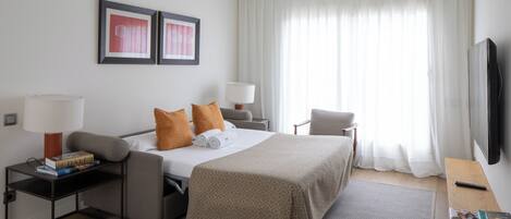 A hotel room with a bed, a desk, a chair, a TV, and a window with curtains.