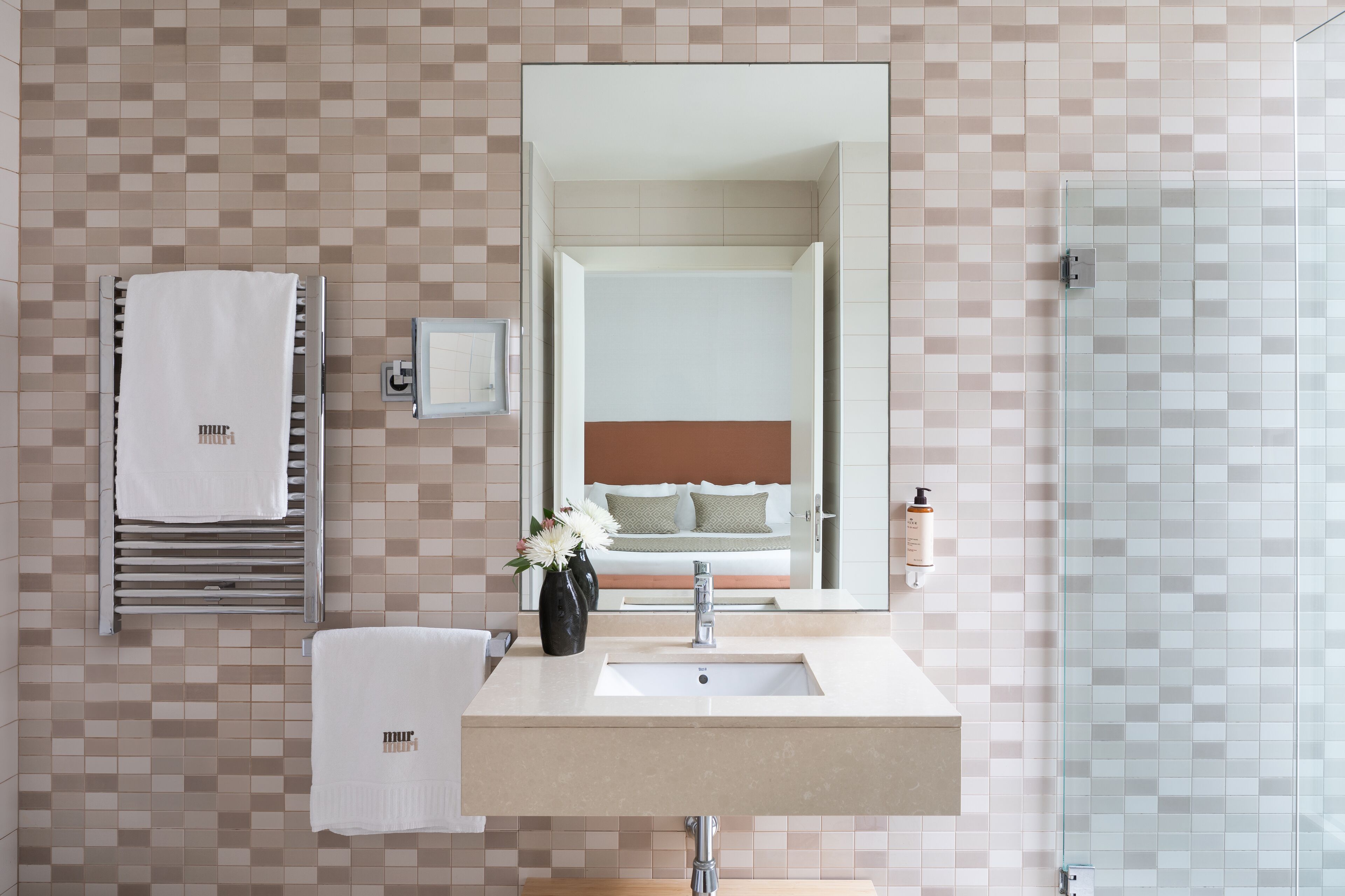 A modern bathroom with a tiled backsplash, a large mirror, a sink, and a glass shower enclosure.