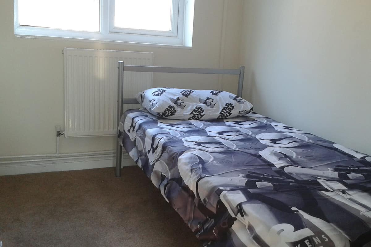 A small, single-bed room with a metal frame, a radiator, and a window.