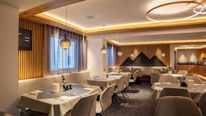 A modern dining area with tables set for service, wooden paneling on the walls, and pendant lighting. - Hotel Chasa Sulai (Ischgl)