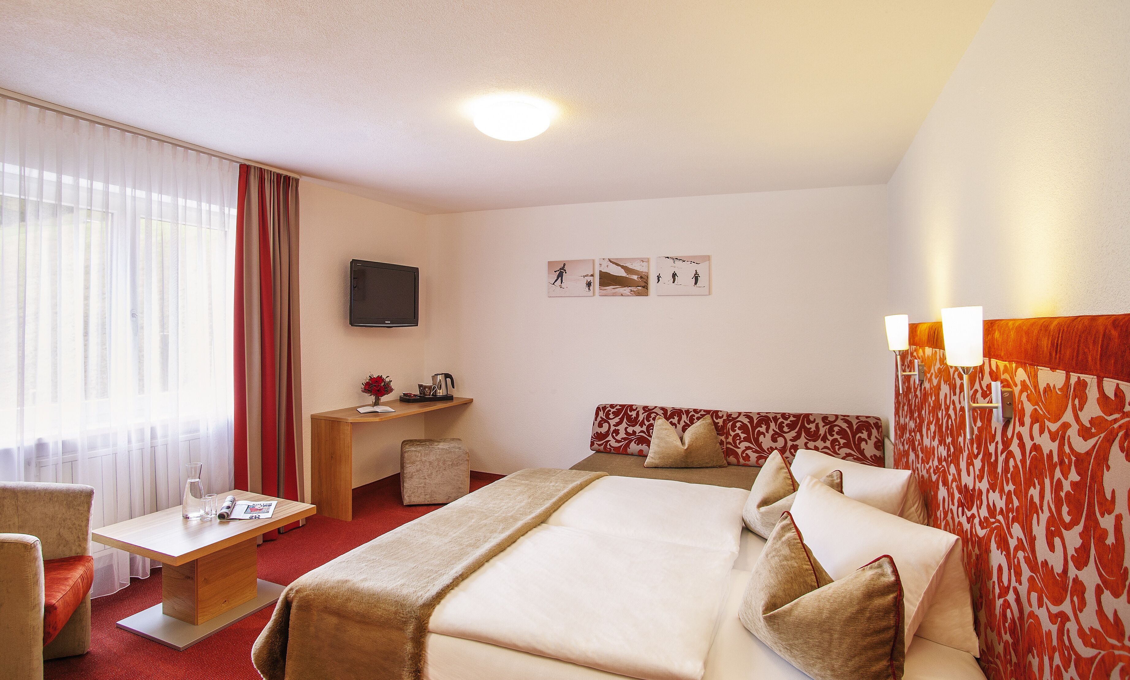 Una habitación de hotel con cama, escritorio, silla, televisor y ventana con cortinas.