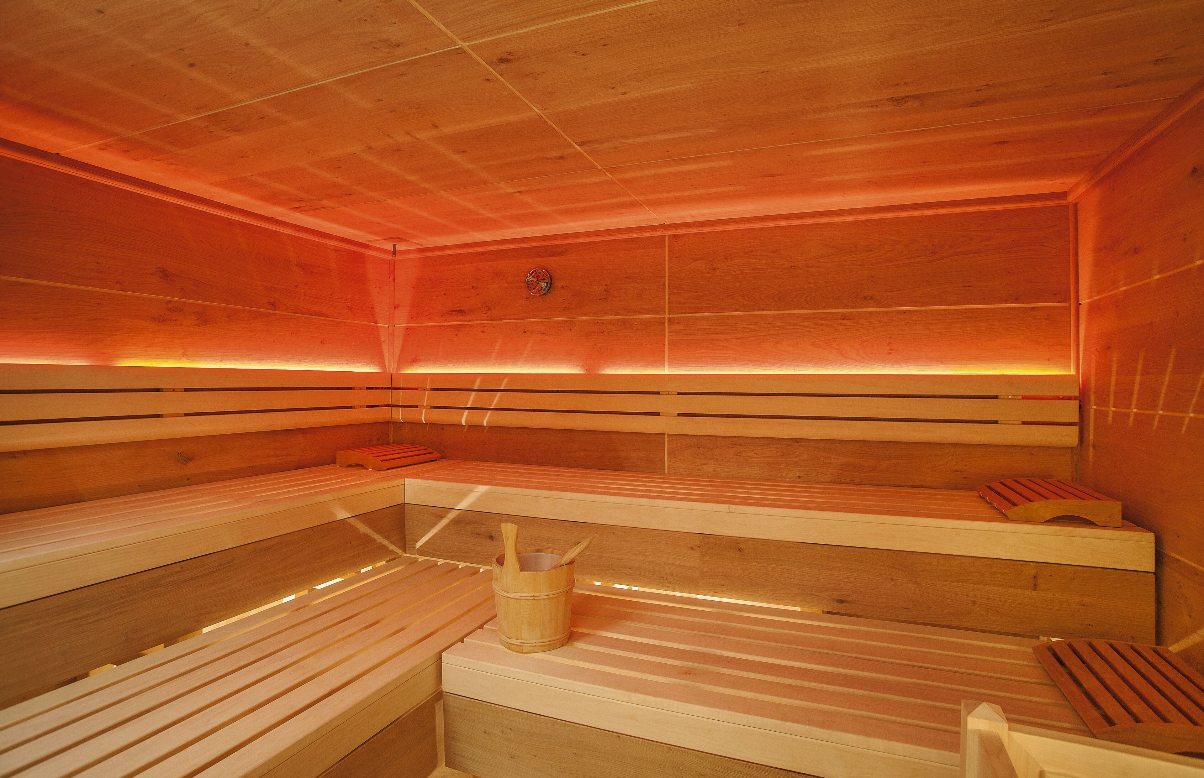 Un sauna avec des bancs en bois, un seau en bois et un radiateur fixé au mur.