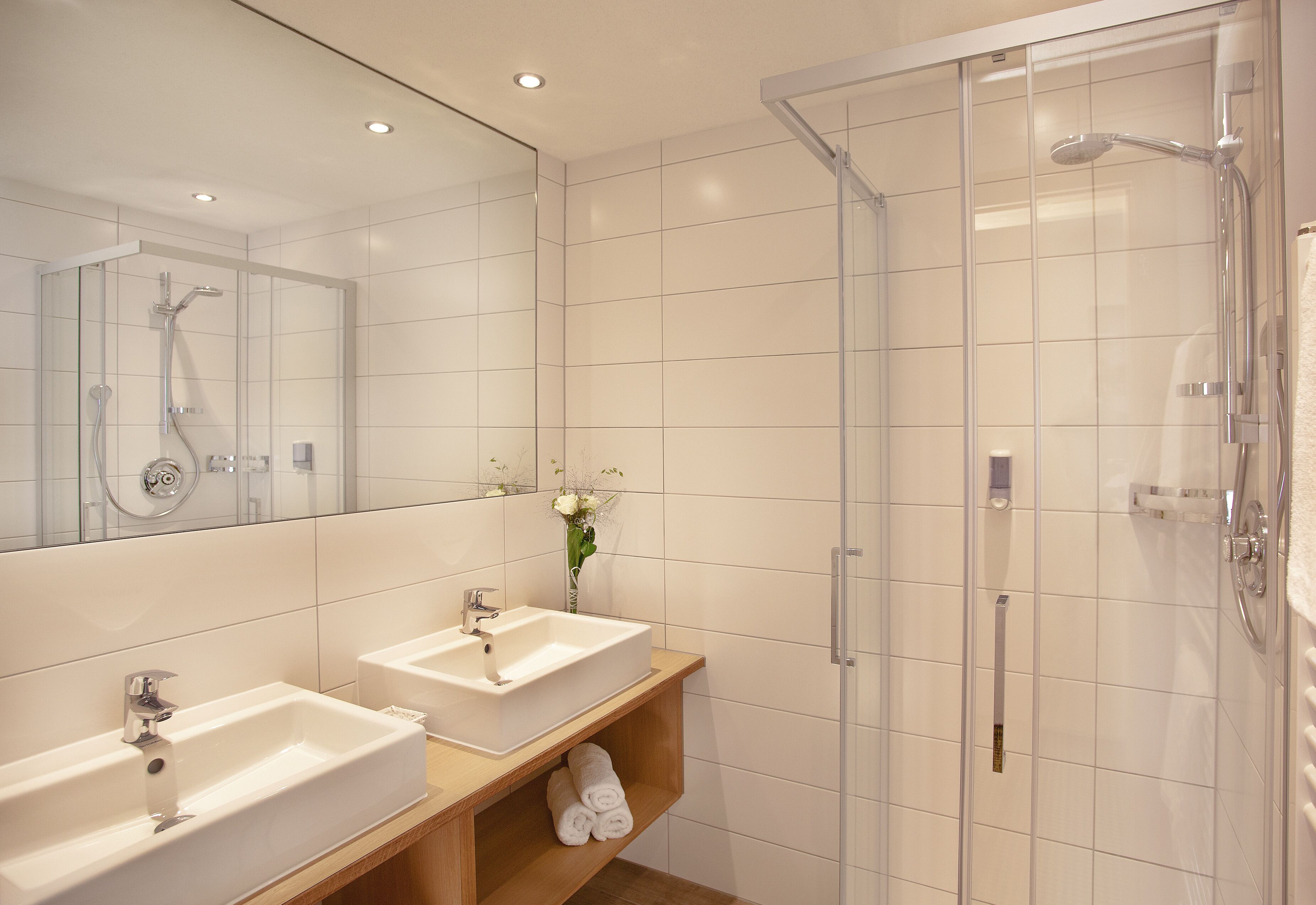 A modern bathroom with two sinks, a glass shower enclosure, and a mirror reflecting the shower area.