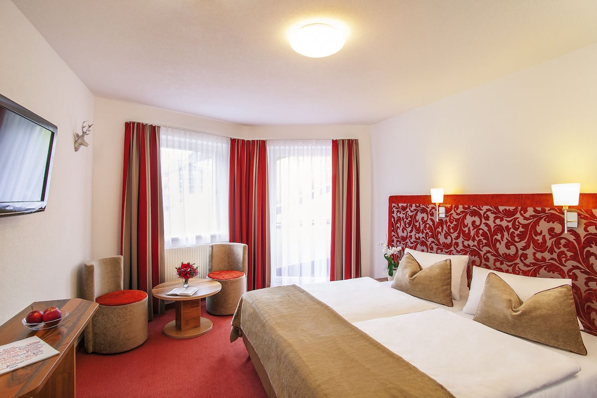 Habitación de hotel con cama, escritorio, silla, mesita y televisor en la pared.