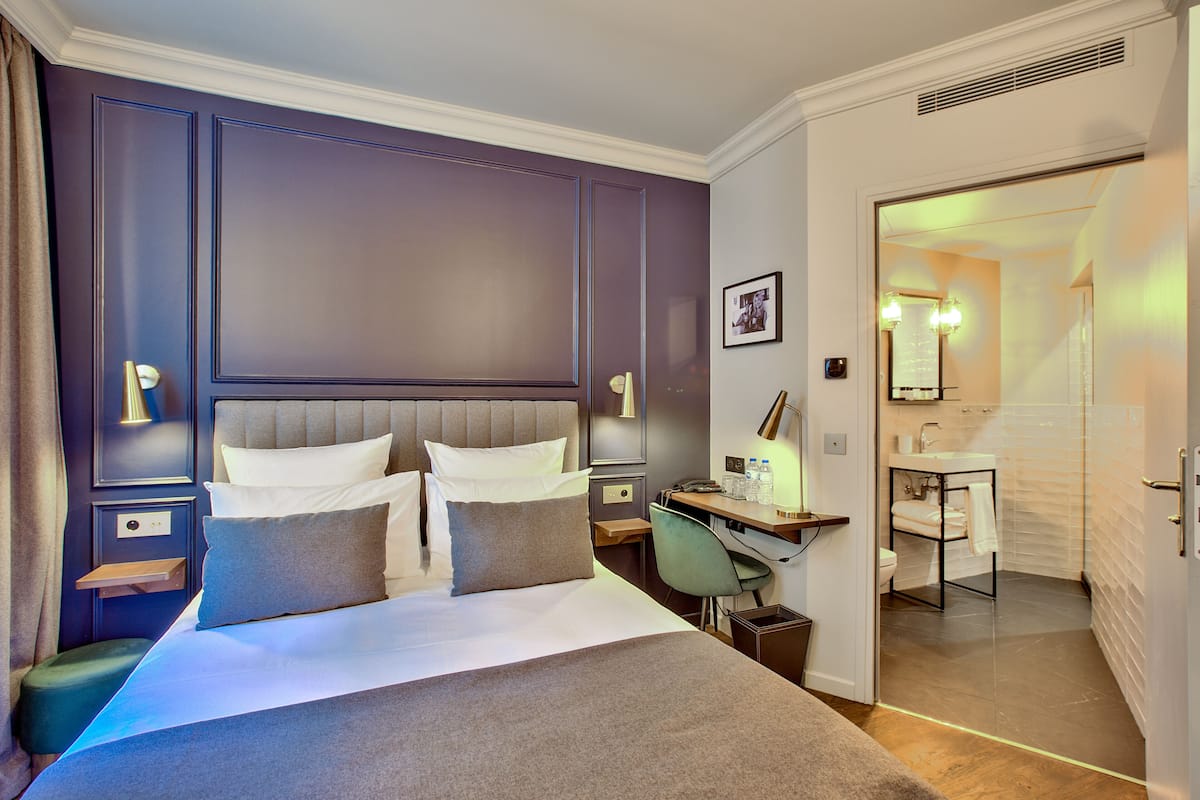 A modern hotel room with a large bed, a desk, and a bathroom visible through an open door.