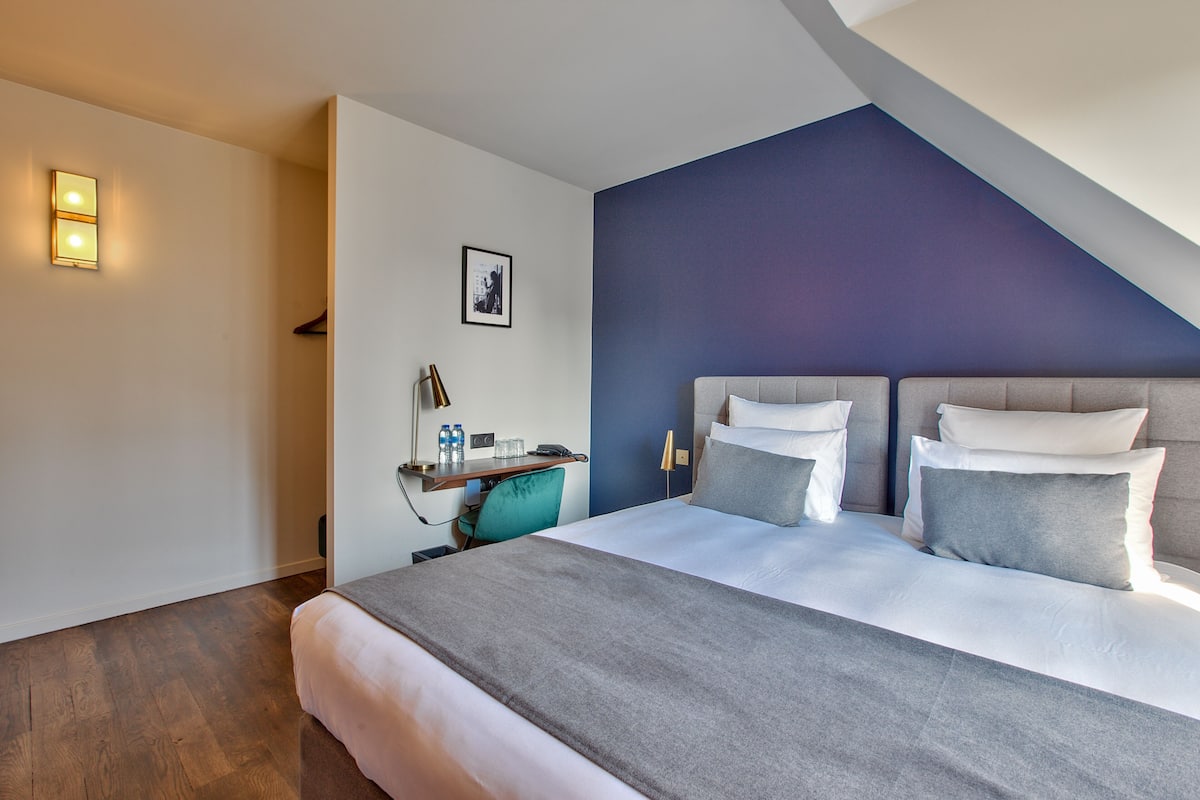 A modern hotel room with a large bed, a desk with a chair, and a blue accent wall.