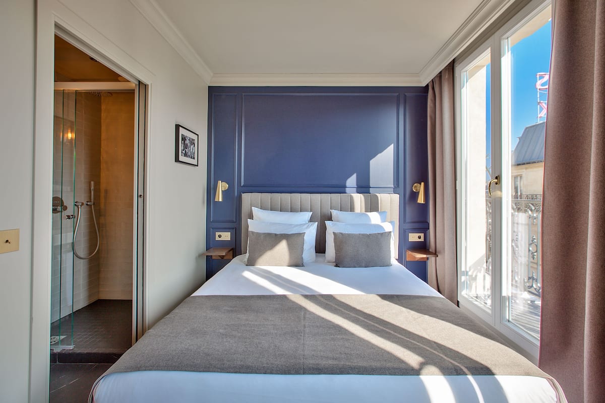 A hotel room with a large bed, a glass shower enclosure, and a view of the city.