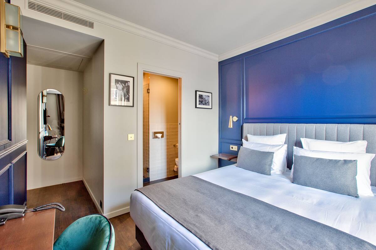 A hotel room with a large bed, a bedside table, a mirror, and a bathroom door.