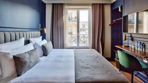 Une chambre d’hôtel avec un lit, un bureau, une chaise, une télévision et une vue sur la ville par la fenêtre.