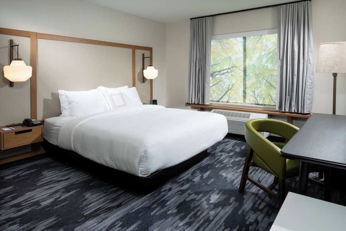 Ein Hotelzimmer mit einem großen Bett, einem Schreibtisch, einem Stuhl und einem Vorhangfenster.