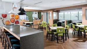 A modern restaurant with a central island, green chairs, and wooden flooring.