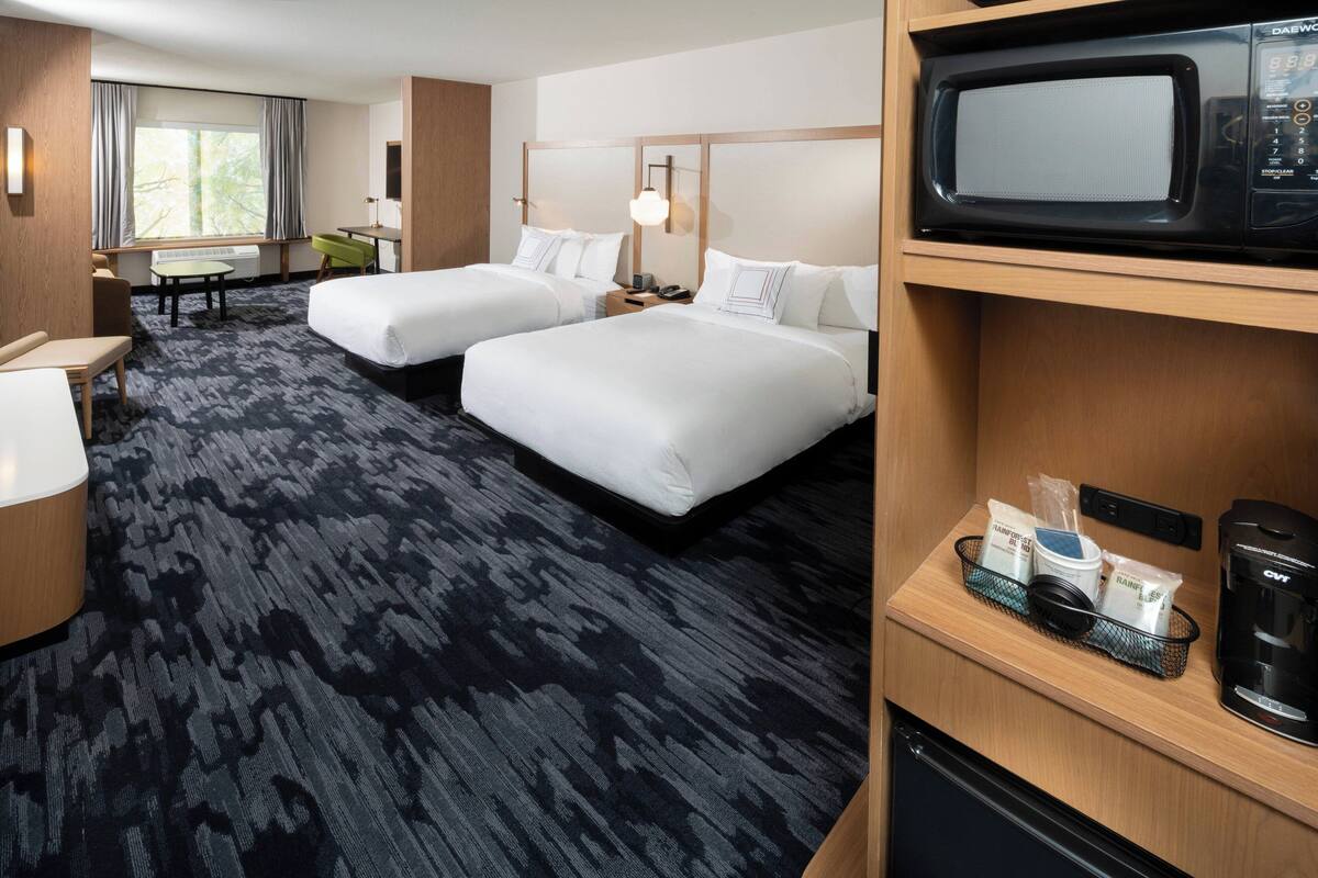 Ein Hotelzimmer mit zwei Betten, einem Schreibtisch, einem Stuhl, einer Mikrowelle und einer Kaffeemaschine.