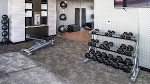 A fitness center with exercise equipment, a mirrored wall, and a television.