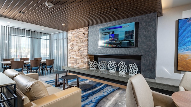 A modern lounge area with leather sofas, a glass-top coffee table, and a flat-screen TV mounted on a stone wall.