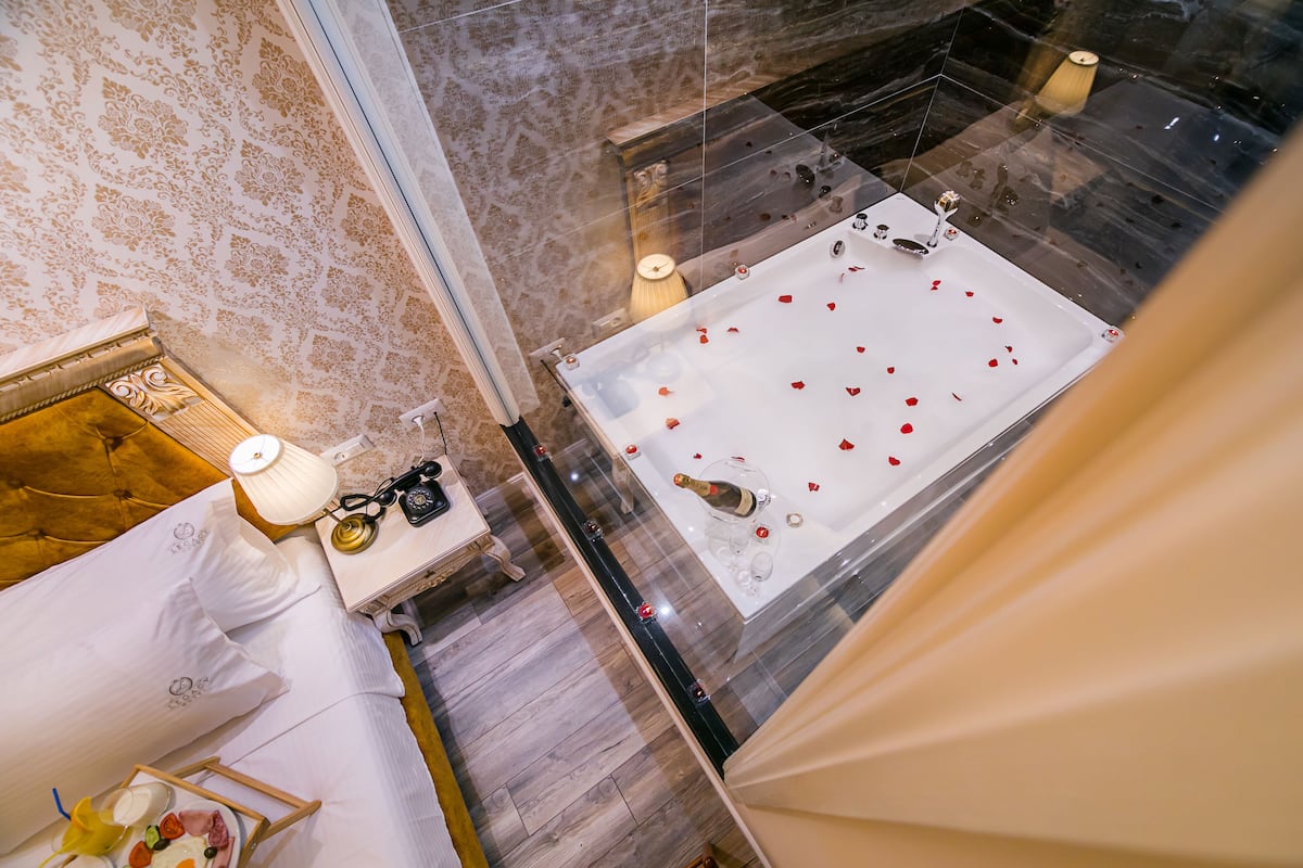 A luxurious bathroom with a large bathtub, marble walls, and a wooden floor.
