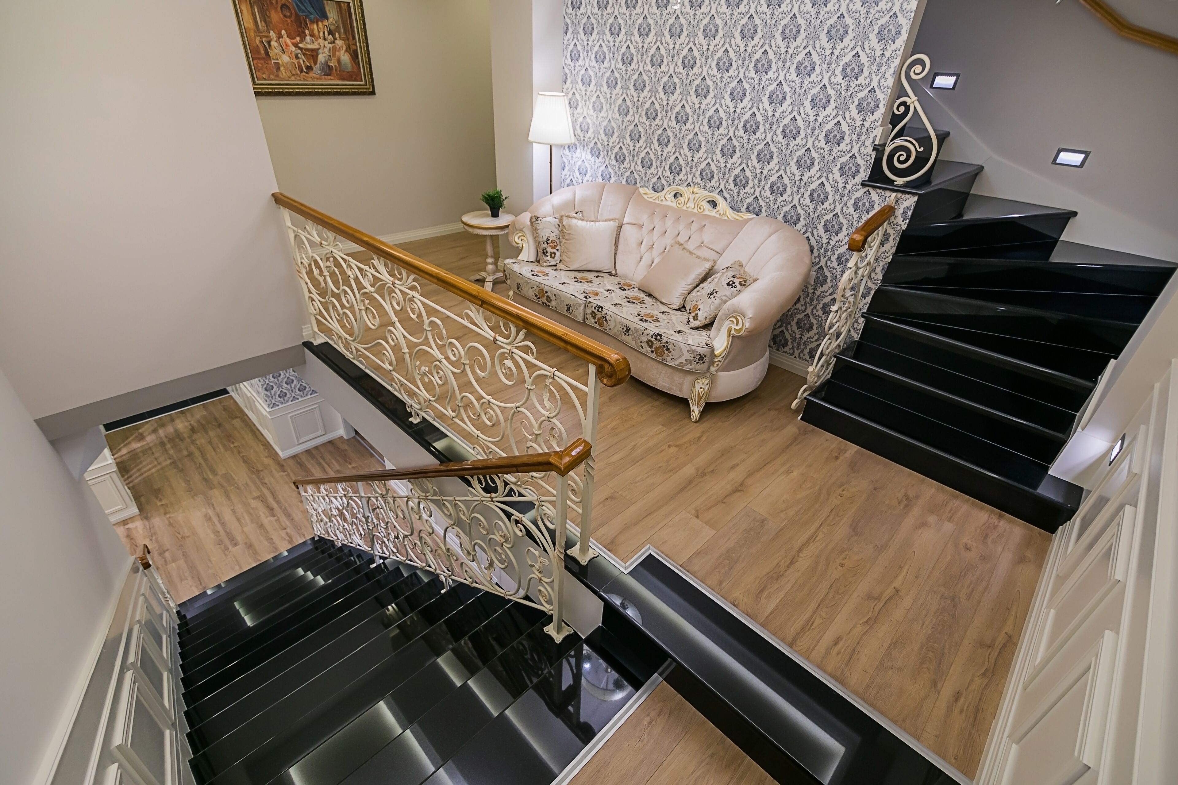 A staircase with a white railing, a beige sofa with floral upholstery, and a patterned wallpaper wall.