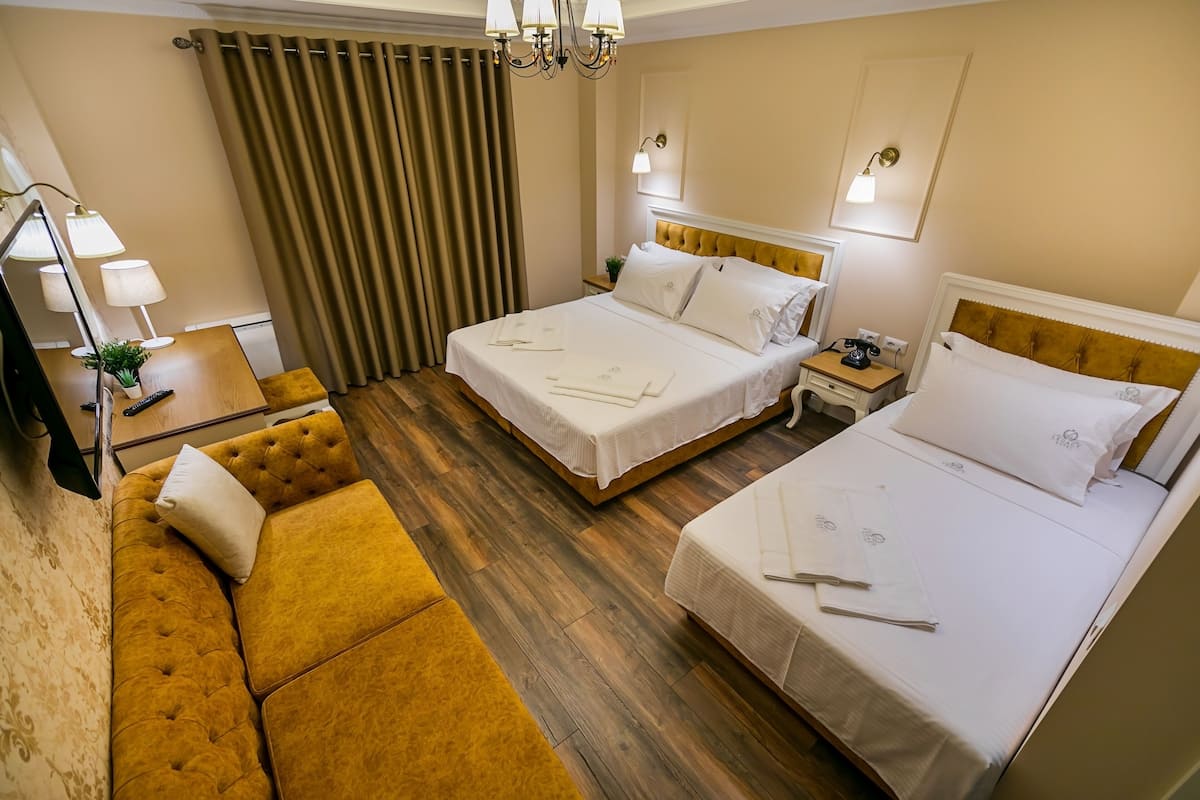 A hotel room with two beds, a sofa, a wooden floor, and a chandelier.