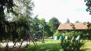 A residential backyard with a swing set, a small house with a tiled roof, and a neatly trimmed lawn.