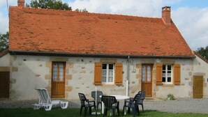 Un bâtiment en pierre avec un toit en tuiles, une table entourée de chaises et une pelouse devant.