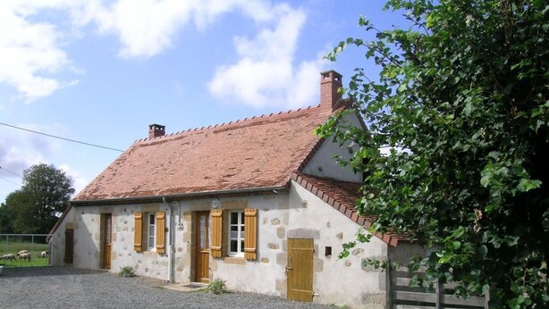 Une maison de campagne en pierre, avec un toit en tuiles, des volets en bois et une allée gravillonnée.