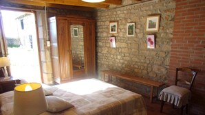 Une chambre à coucher comprenant un lit, un banc, une chaise, une lampe et un mur en pierre orné de tableaux encadrés.