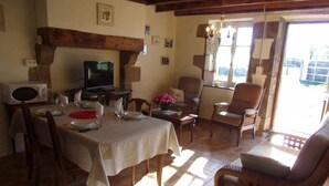 Un coin repas avec une table dressée pour quatre personnes, un téléviseur et une fenêtre avec des rideaux.