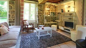 A cozy living room with a stone wall, wooden beams, a sofa, a coffee table, a TV, and a bookshelf.