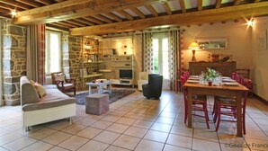 A spacious living area with a high wooden ceiling, stone walls, a fireplace, a dining table set for six, and a comfortable sofa.