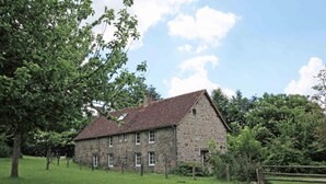 A stone building with a sloped roof, surrounded by a grassy field and trees.