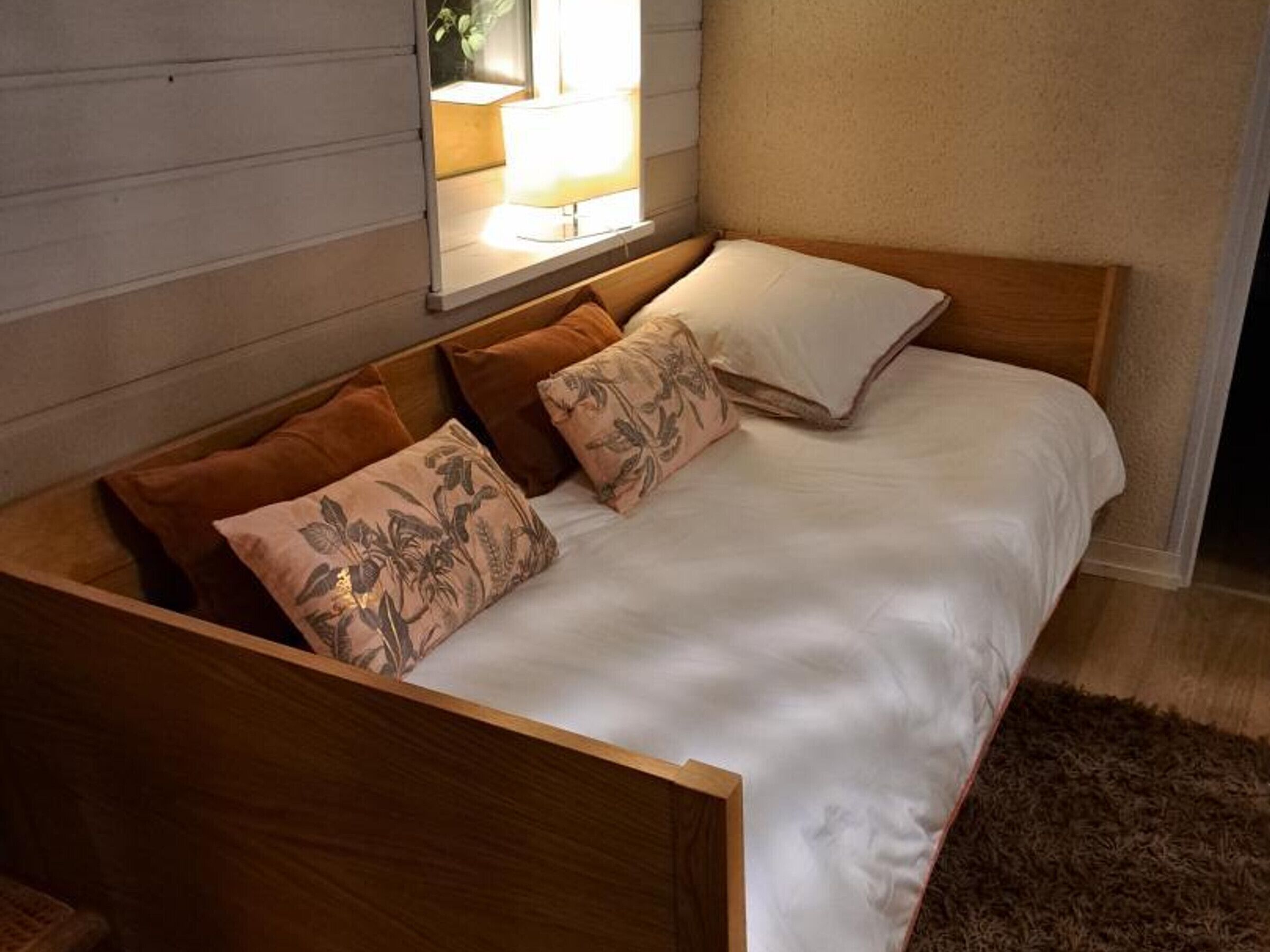 Ein hölzernes Bett mit weißer Bettwäsche und zwei gemusterten Kissen.