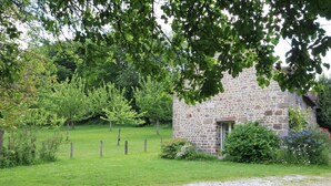 A stone building with a small window, surrounded by a grassy field and trees.
