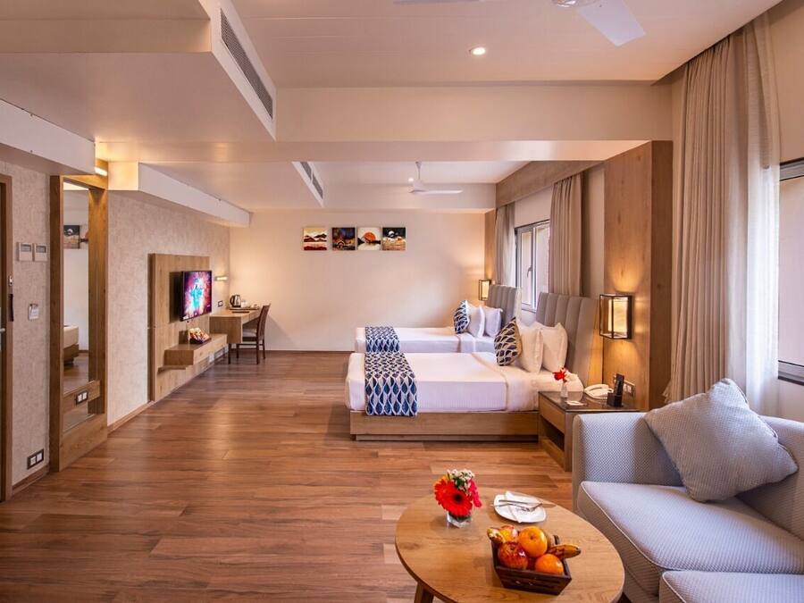 A hotel room with a bed, a sofa, a TV, a desk, and a coffee table with fruit.