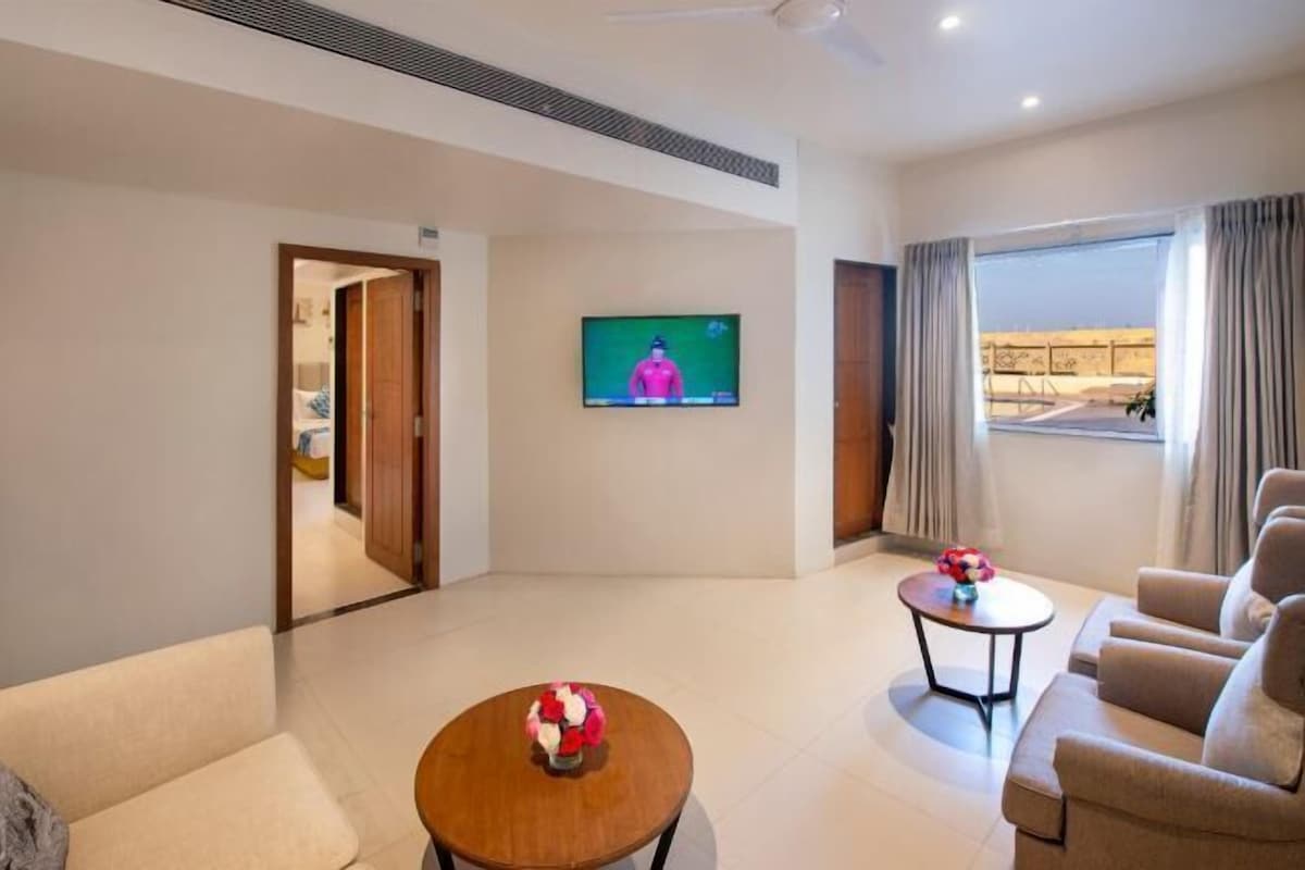 Una habitación de hotel con televisión, una mesa de centro redonda, un sofá y un ventanal grande.