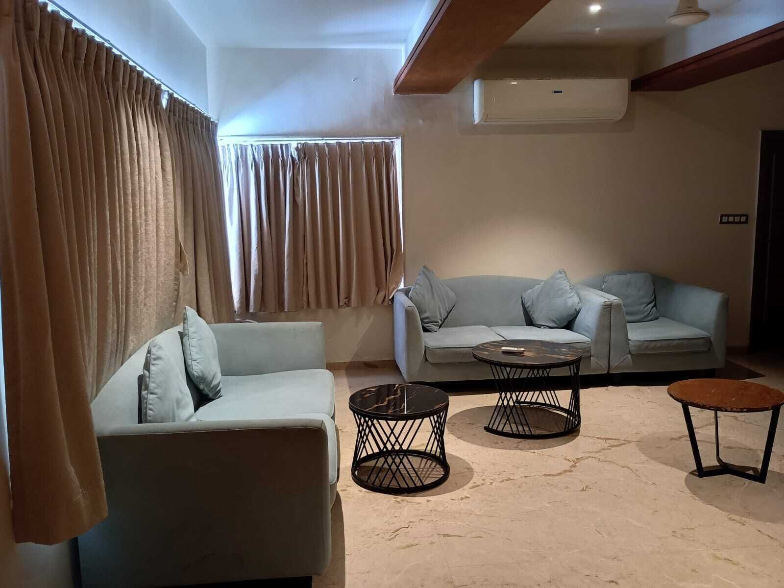 A living room with a sofa, two coffee tables, and a window with curtains.