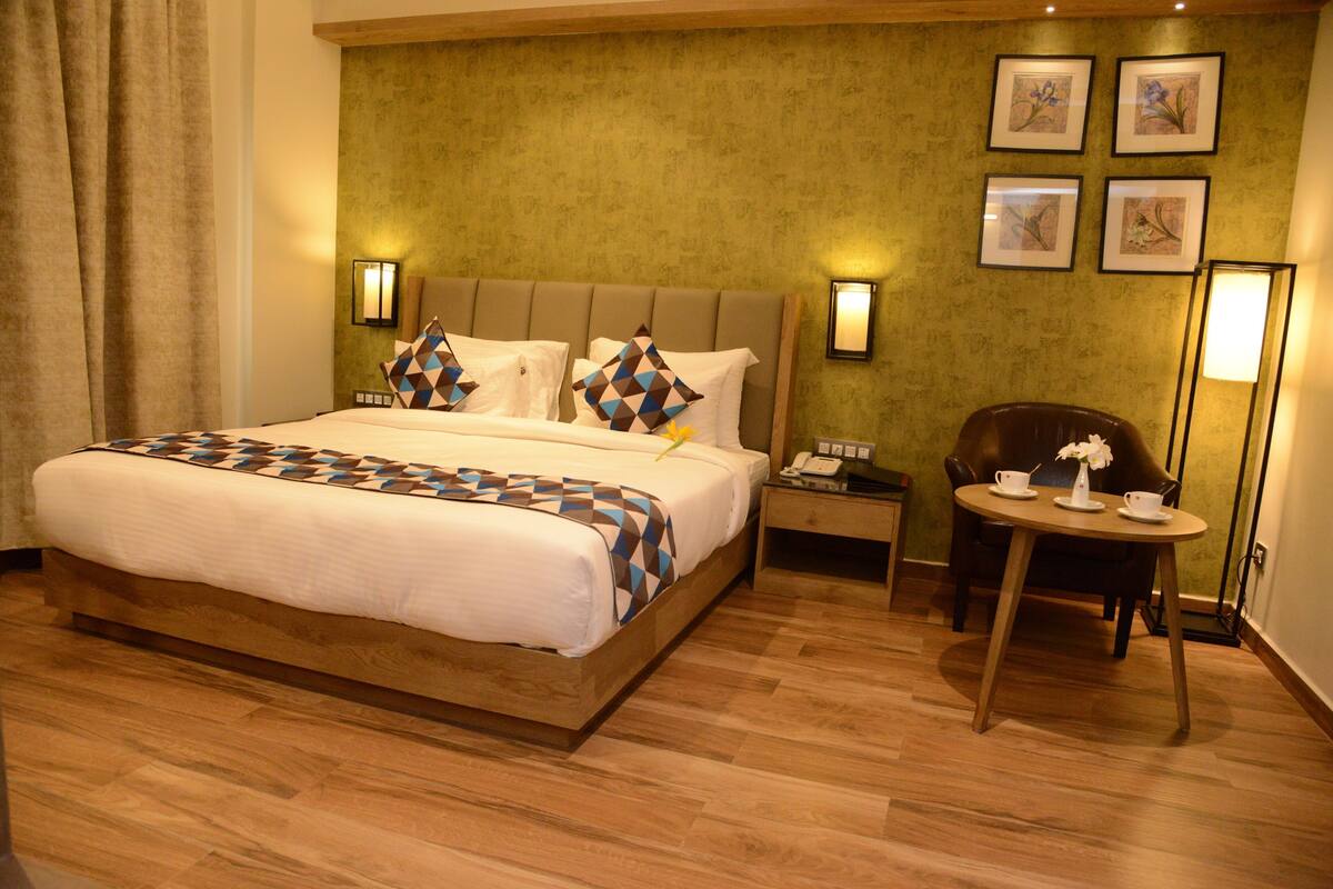 A hotel room with a bed, bedside tables, a chair, and a small table with cups and a vase.