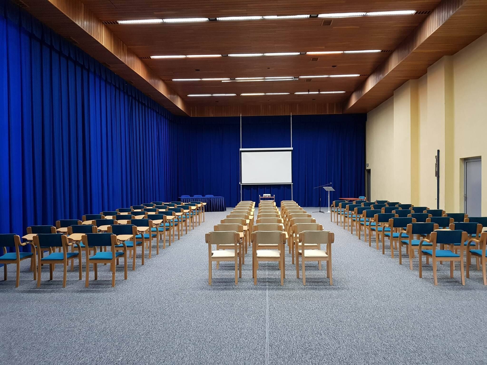 Ein Konferenzraum mit Reihen von Stühlen, einer Projektionsleinwand und einem Rednerpult.