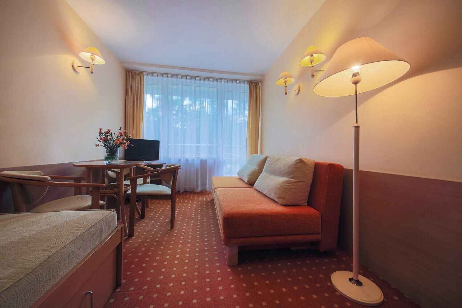 A hotel room with a sofa, a desk with a computer, a TV, and a lamp.