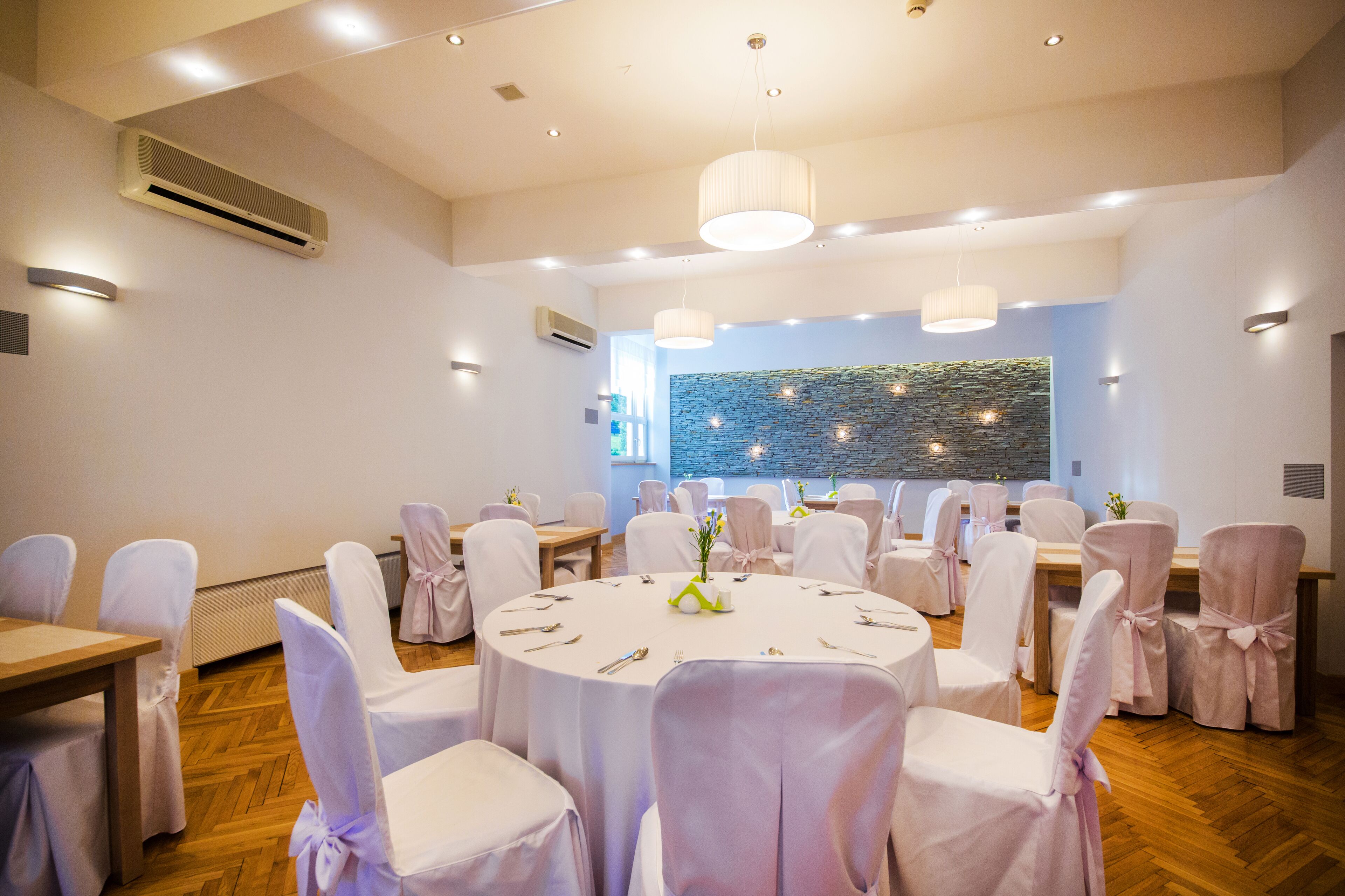 A conference room with round tables, white chairs, and a stone wall in the background.