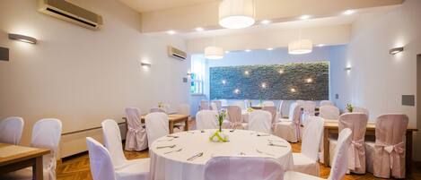 A conference room with round tables, white chairs, and a stone wall in the background.