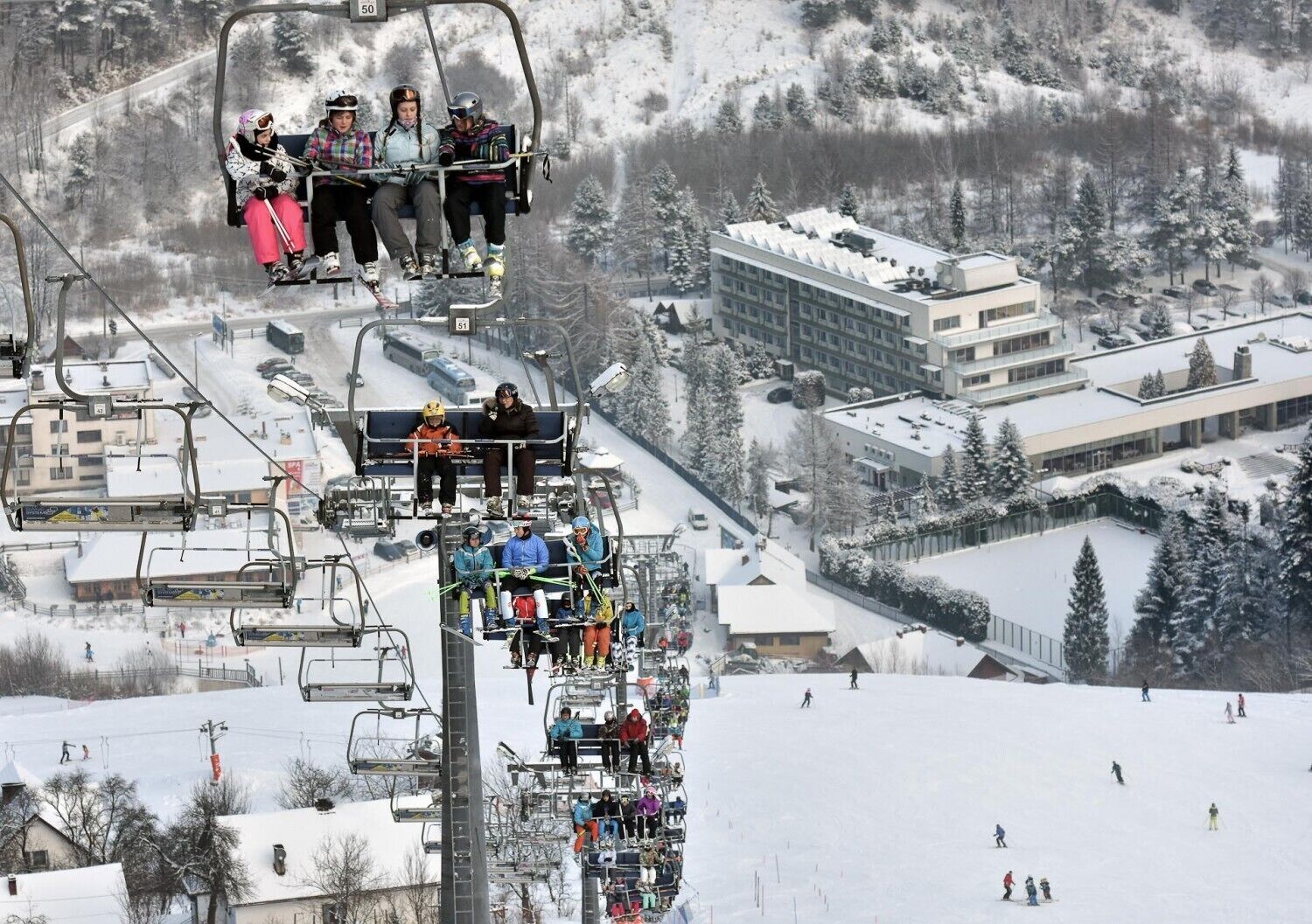 Eine Seilbahn mit Skifahrern und ein modernes Gebäude mit flachem Dach und großen Fenstern.