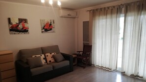 A living room with a sofa, a wooden side table, a chair, and two wall-mounted paintings. - Estudios Solmar 1º, Solo Familias! (Playa de Gandía)