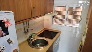 A compact kitchen with wooden cabinets, a stainless steel sink, and a built-in dishwasher. - Estudios Solmar 1º, Solo Familias! (Playa de Gandía)