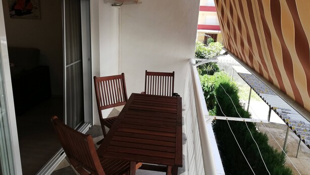 A balcony with a wooden table and chairs, a sliding glass door, and a striped awning. - Estudios Solmar 1º, Solo Familias! (Playa de Gandía)