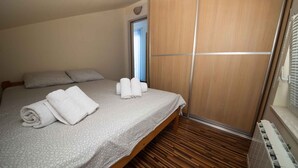 Cama bem arrumada com toalhas dobradas, piso de madeira e porta de madeira deslizante.