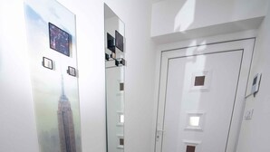 Um corredor com piso de madeira, uma porta de design moderno e um espelho grande refletindo o corredor.