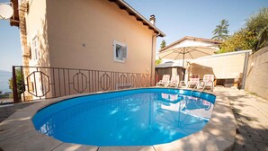 Piscina com deck revestido, área de varanda coberta com cadeiras e vista para o mar.